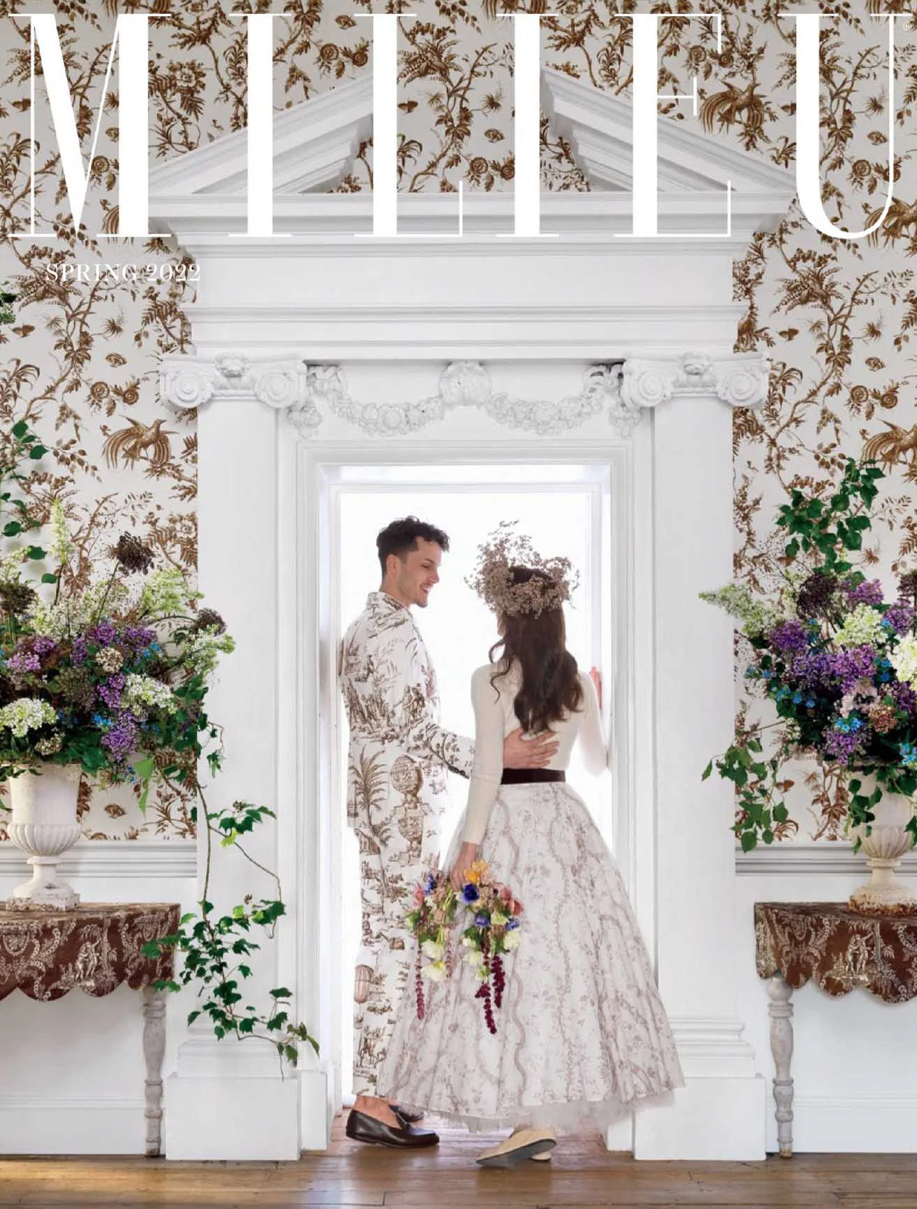 Couple in floral setting, dressed elegantly, surrounded by flowers.