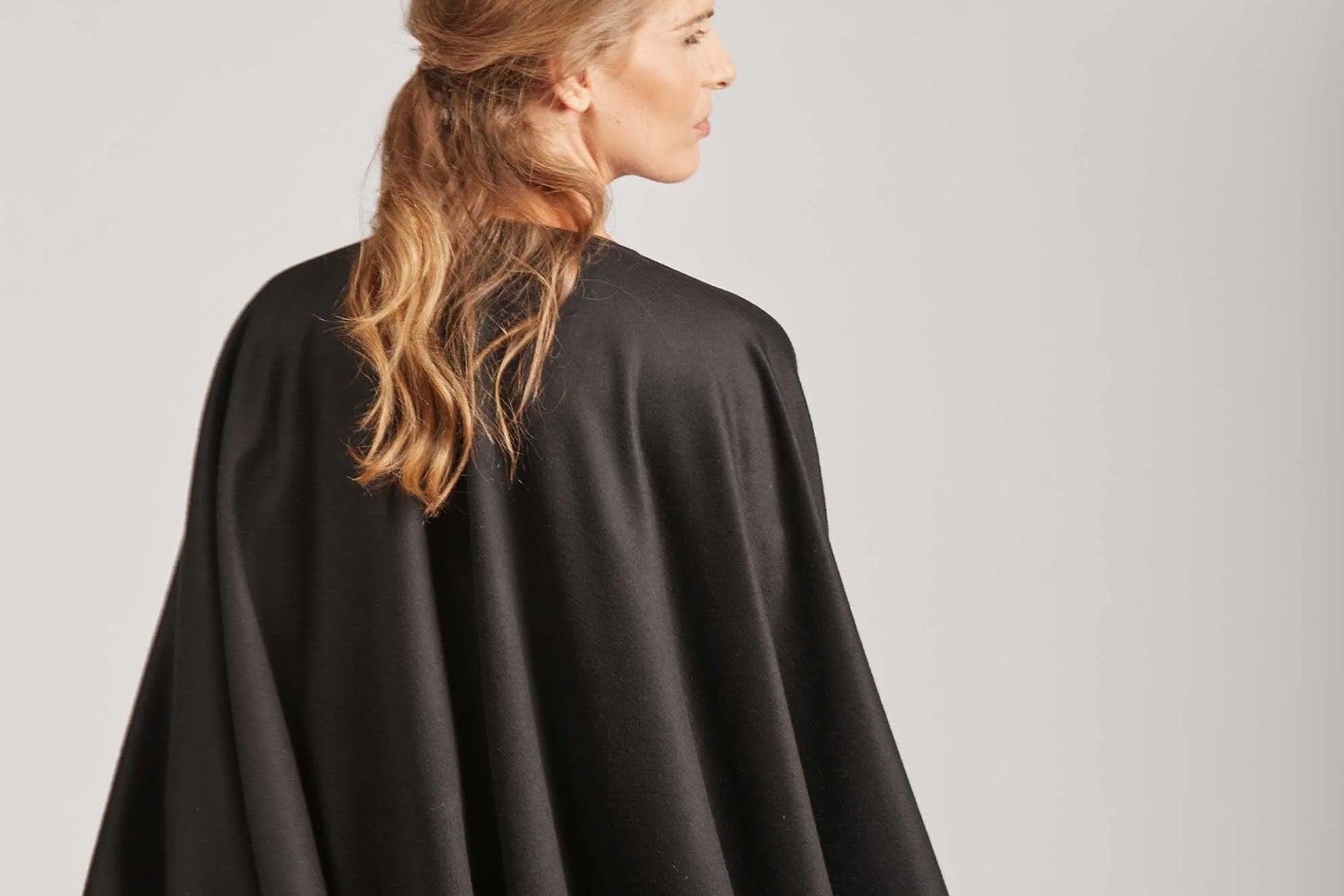 Woman with long hair wearing a black cape, viewed from behind.