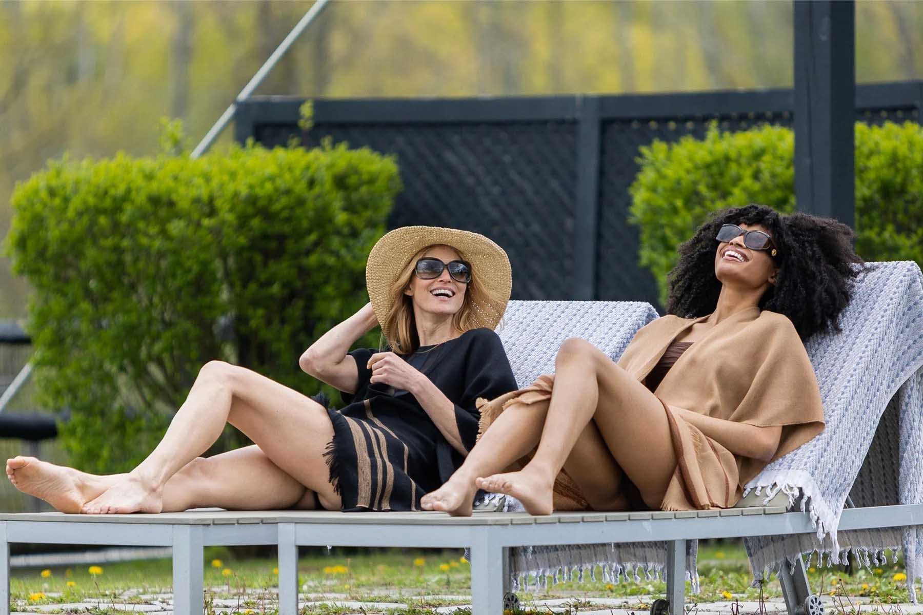 Two women relaxing in lounge chairs, wearing sunglasses, enjoying a sunny day.