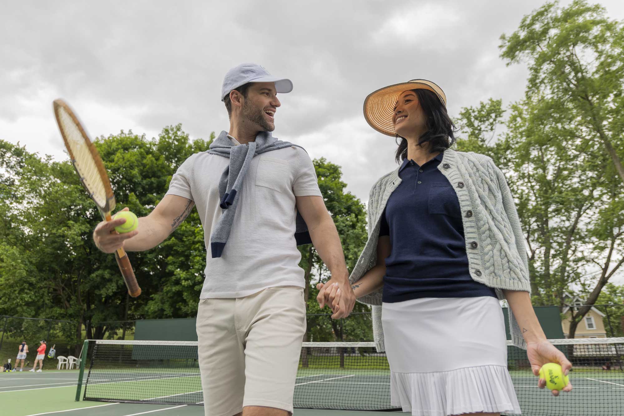 A couple holding hands on a tennis court, smiling at each other.
