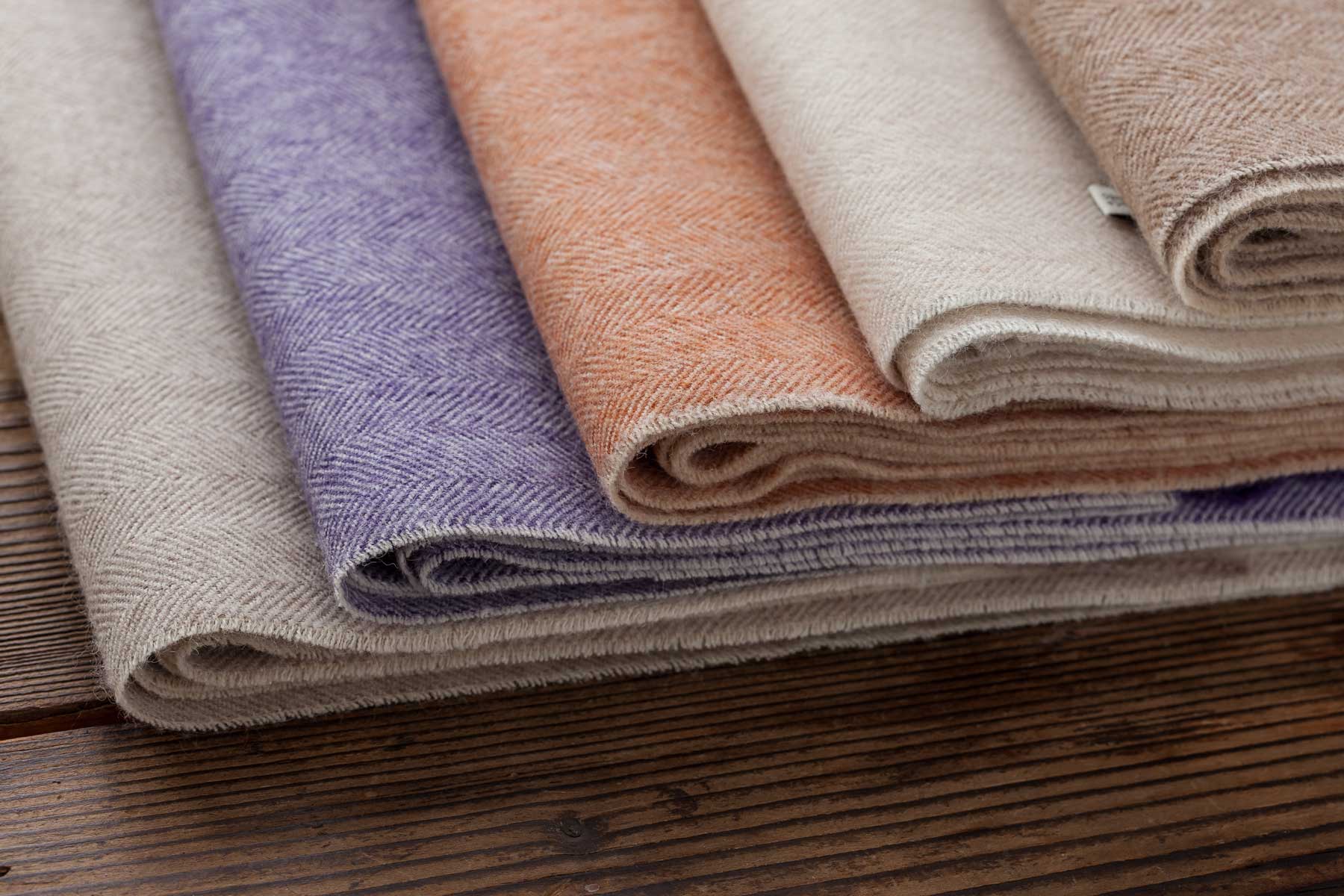 Various rolls of fabric in pastel colors on a wooden surface.