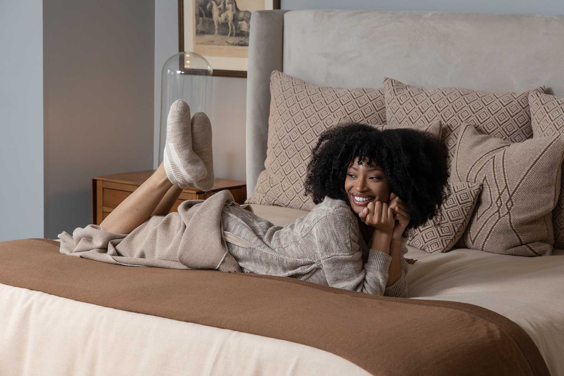 Smiling woman lounging on a bed with decorative pillows.